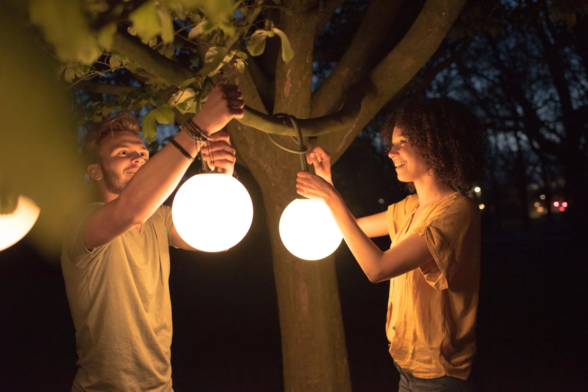 Twee mensen hangen een Hanglamp Bolleke met ronde lichten op in een sfeervolle ruimte